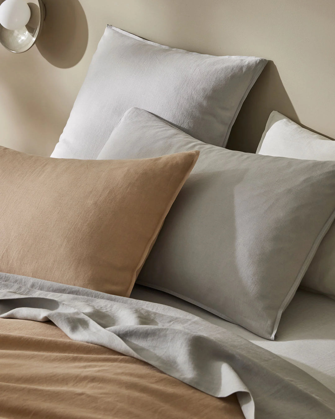 Neutral layered bedding setup featuring linen pillowcases and flat sheet in soft biscuit and silver tones with textured weave, minimalist bedroom styling with warm natural light