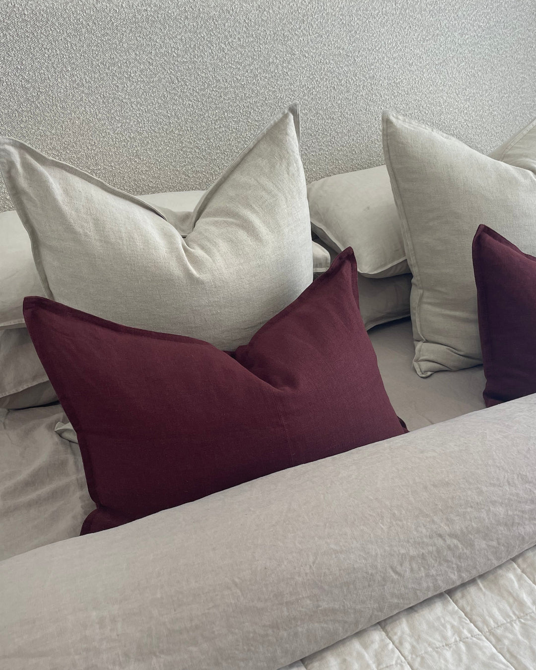 Stack of pillows with maroon and beige colors against a textured wall.
