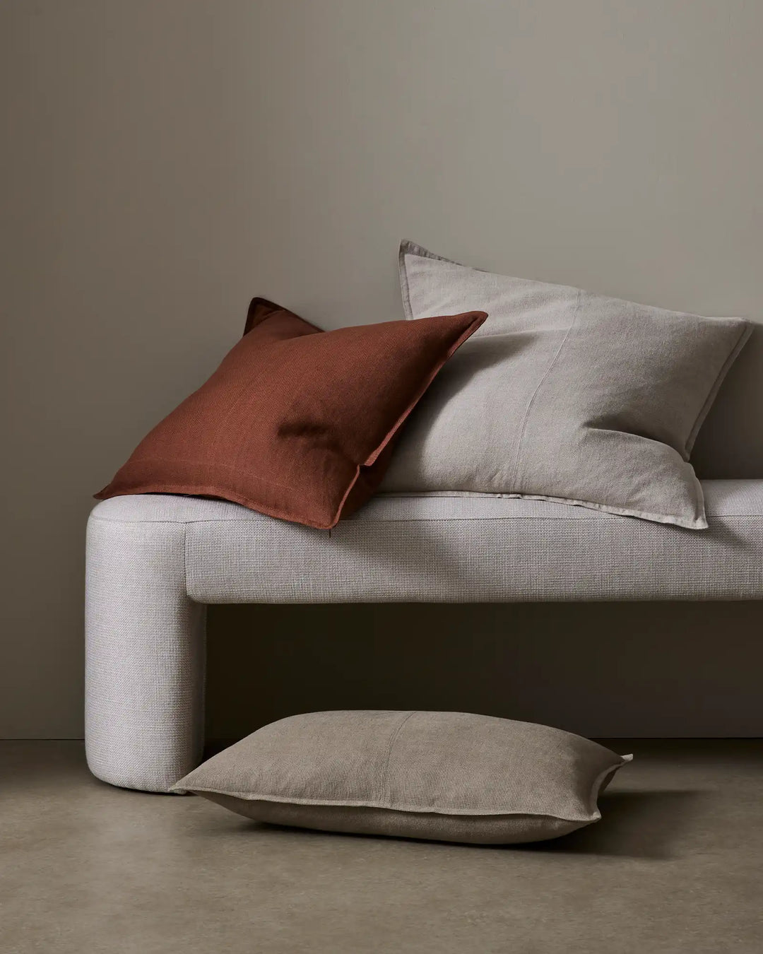 Neutral linen sofa styled with Como cushions in warm terracotta, soft greige and pale stone, creating an earthy minimalist aesthetic with layered textures