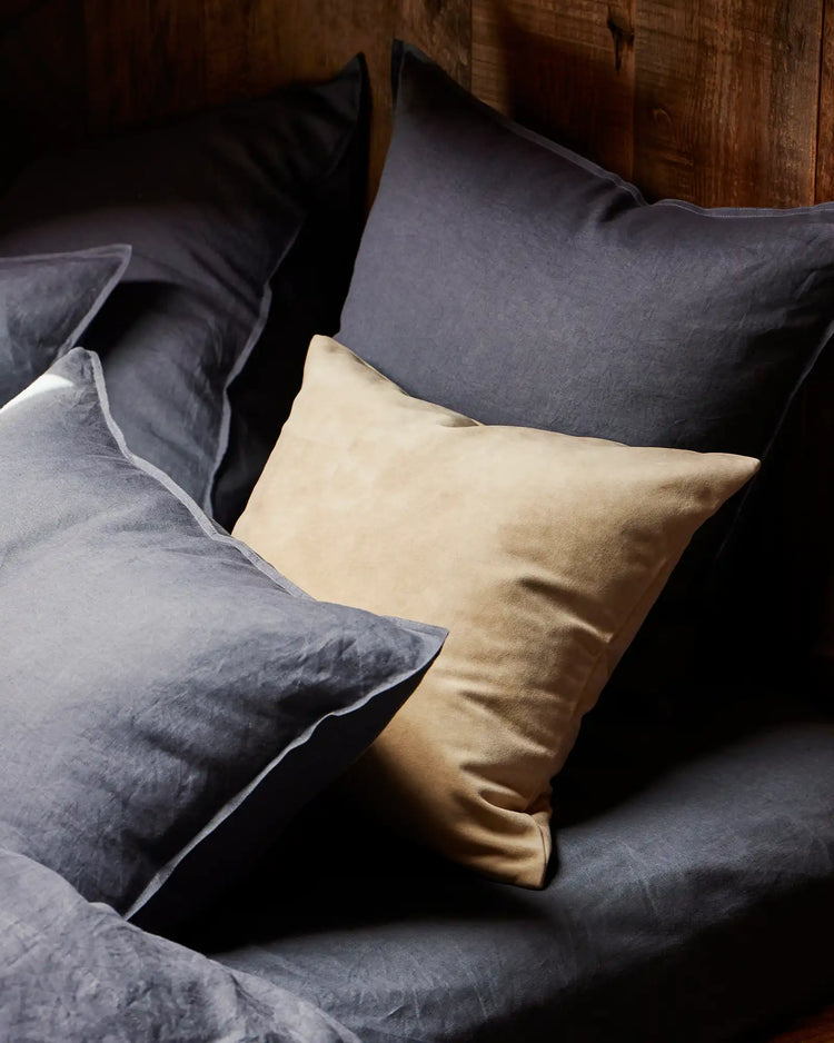 Layered bed styling with Ravello Fitted Sheet and Ravello Pillowcase in denim, cream, and charcoal linen tones against warm timber headboard