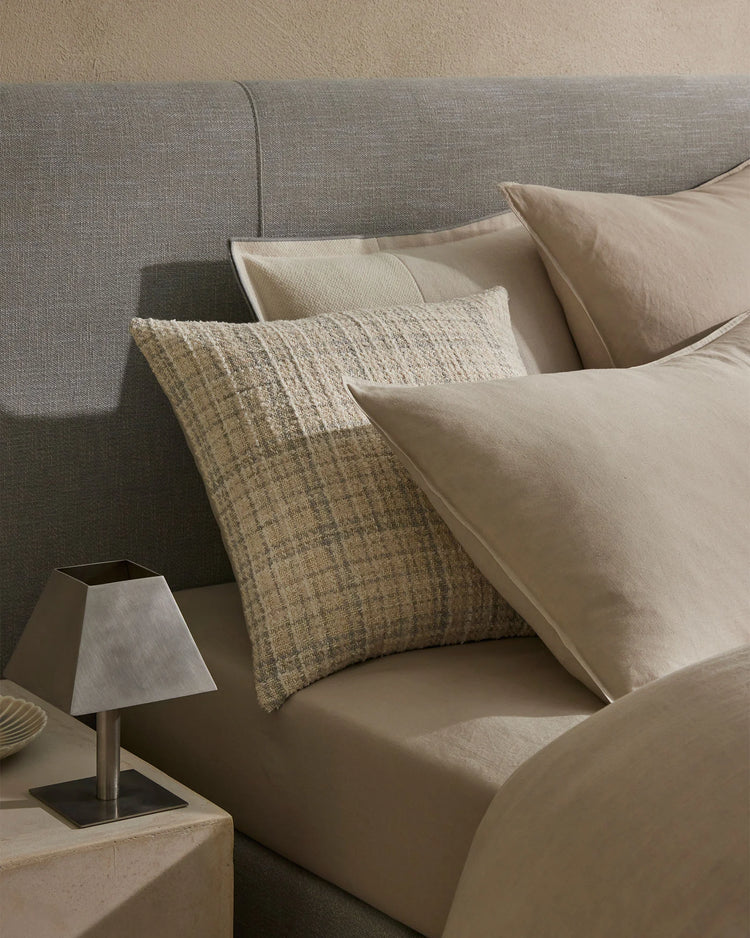 Neutral monochrome sofa styling with layered linen pillowcases and textured cushions in cream, oatmeal and warm taupe tones, creating a serene minimalist aesthetic