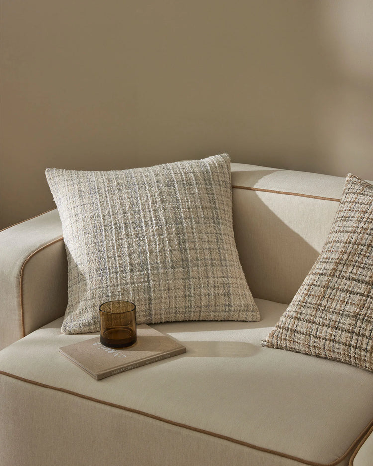 Neutral monochromatic sofa styling with Tripoli cushions in cream and taupe textures, paired with amber glass and natural wood accents against warm beige walls