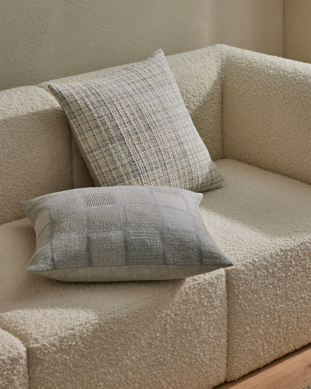 Neutral monochromatic cushions with woven textures layered on a cream boucle armchair, showcasing minimalist geometric patterns in soft linen and cotton blends