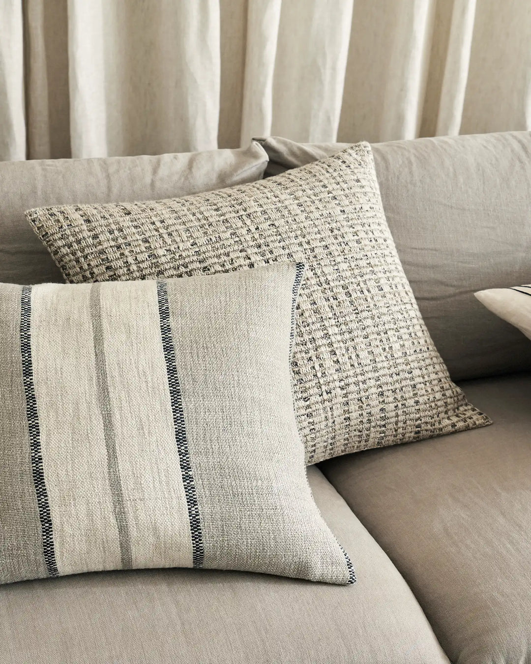 Neutral linen cushions styled on a cream sofa with striped and textured weave details, paired with gauze curtains in warm greige tones