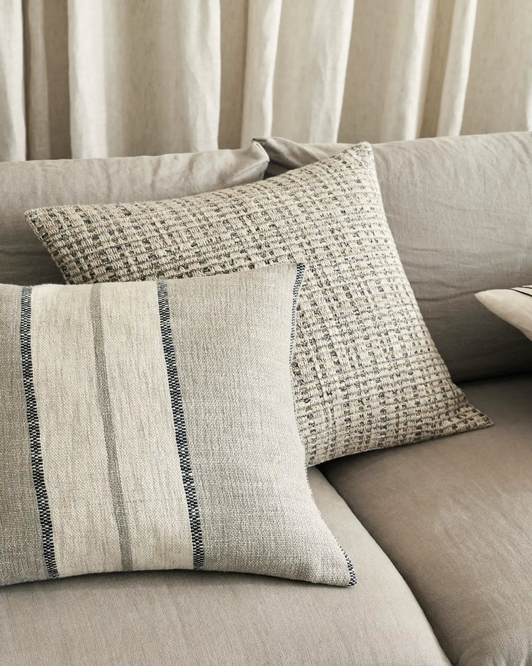 Neutral linen cushions styled on a cream sofa with striped and textured weave details, paired with gauze curtains in warm greige tones