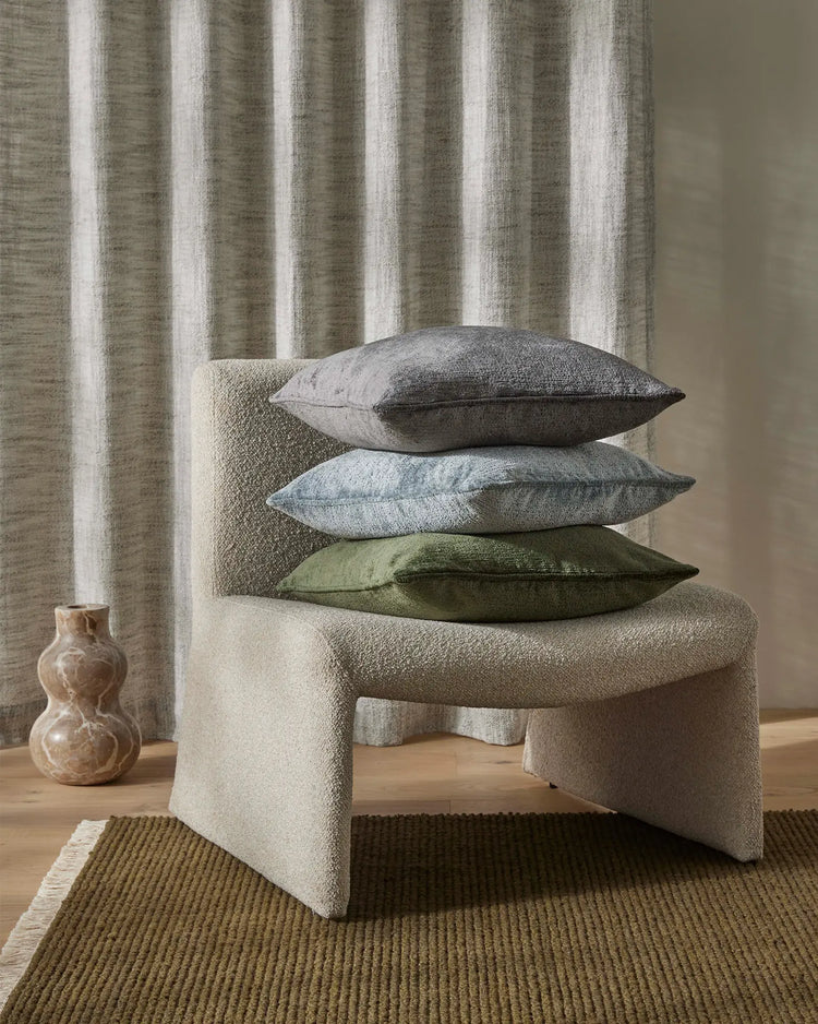 Neutral minimalist styling with stacked Tempo cushions in charcoal, sky blue and forest green on a cream wool bench, vertical striped curtains and moss-toned ribbed rug layered with cream trim.