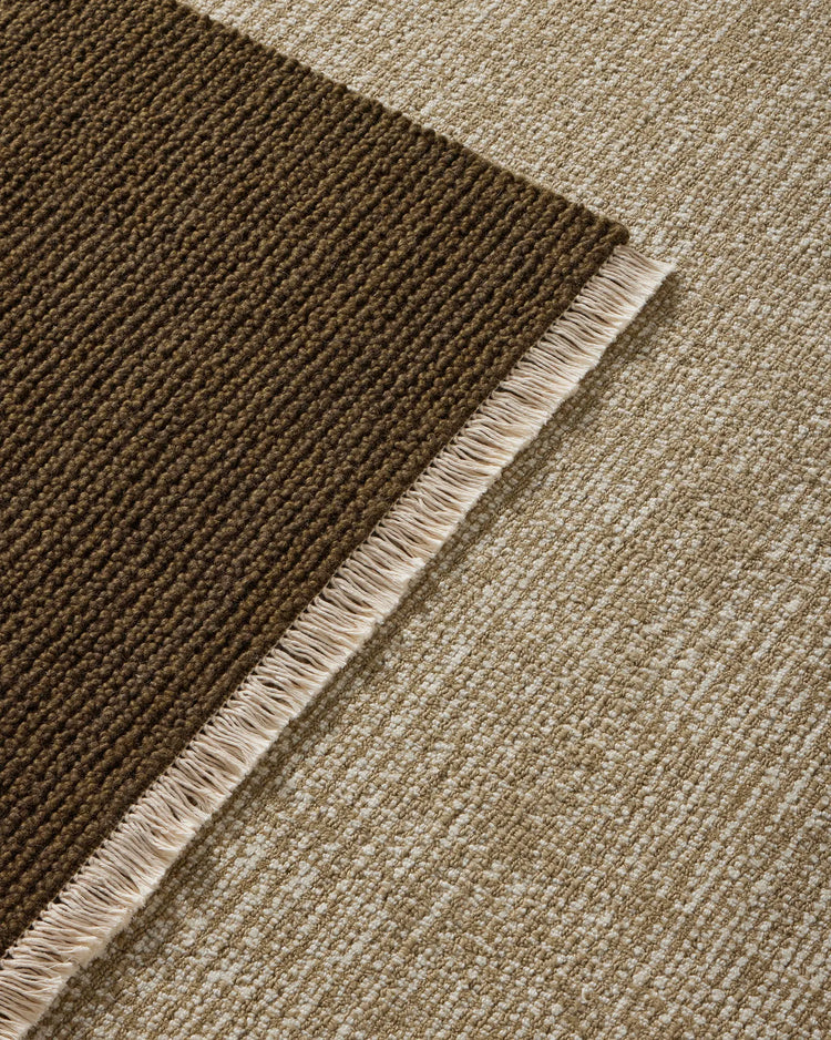 Layered neutral wool rugs in moss and willow tones showcase woven texture and fringed edges, creating warm earthy depth for modern interiors
