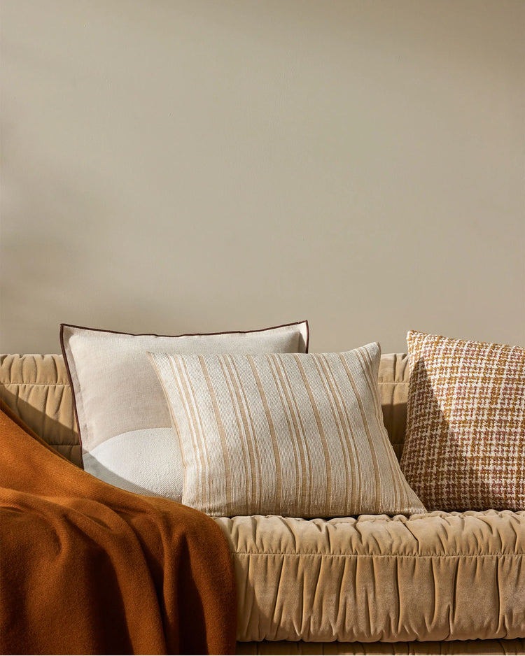 Neutral linen cushions and rust throw on a beige sofa, styled with striped and textured weave pillows for warm, minimalist living room decor