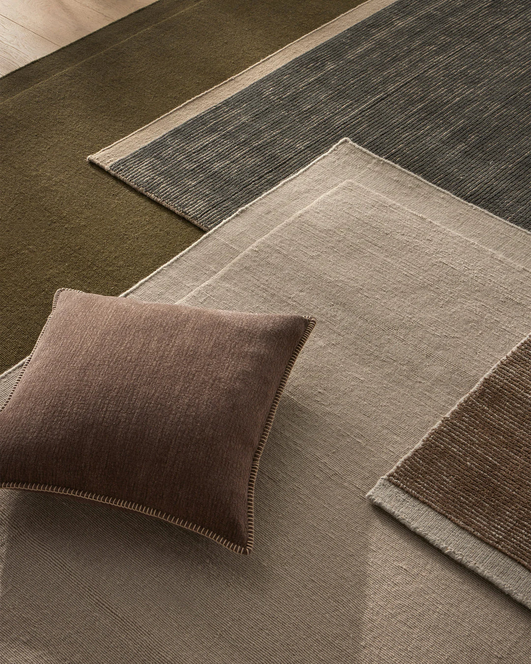 Earthy toned interior styling with Cassio Fog rug, Alba cushion and layered natural textiles in sage green, warm taupe and charcoal with prominent linear weave textures