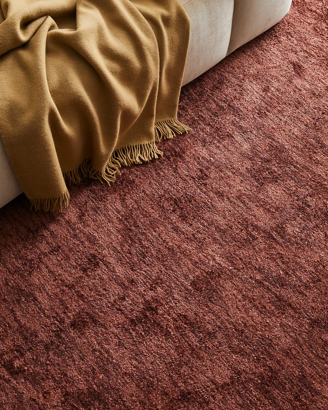 Warm earthy tones of mustard and terracotta create a cohesive interior mood, with a fringed wool throw draped over cream upholstery and a textured bamboo silk rug anchoring the layered seating arrangement.