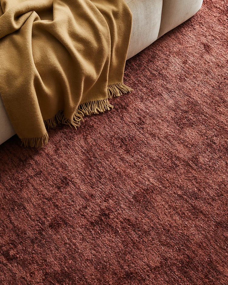 Warm earthy tones of mustard and terracotta create a cohesive interior mood, with a fringed wool throw draped over cream upholstery and a textured bamboo silk rug anchoring the layered seating arrangement.