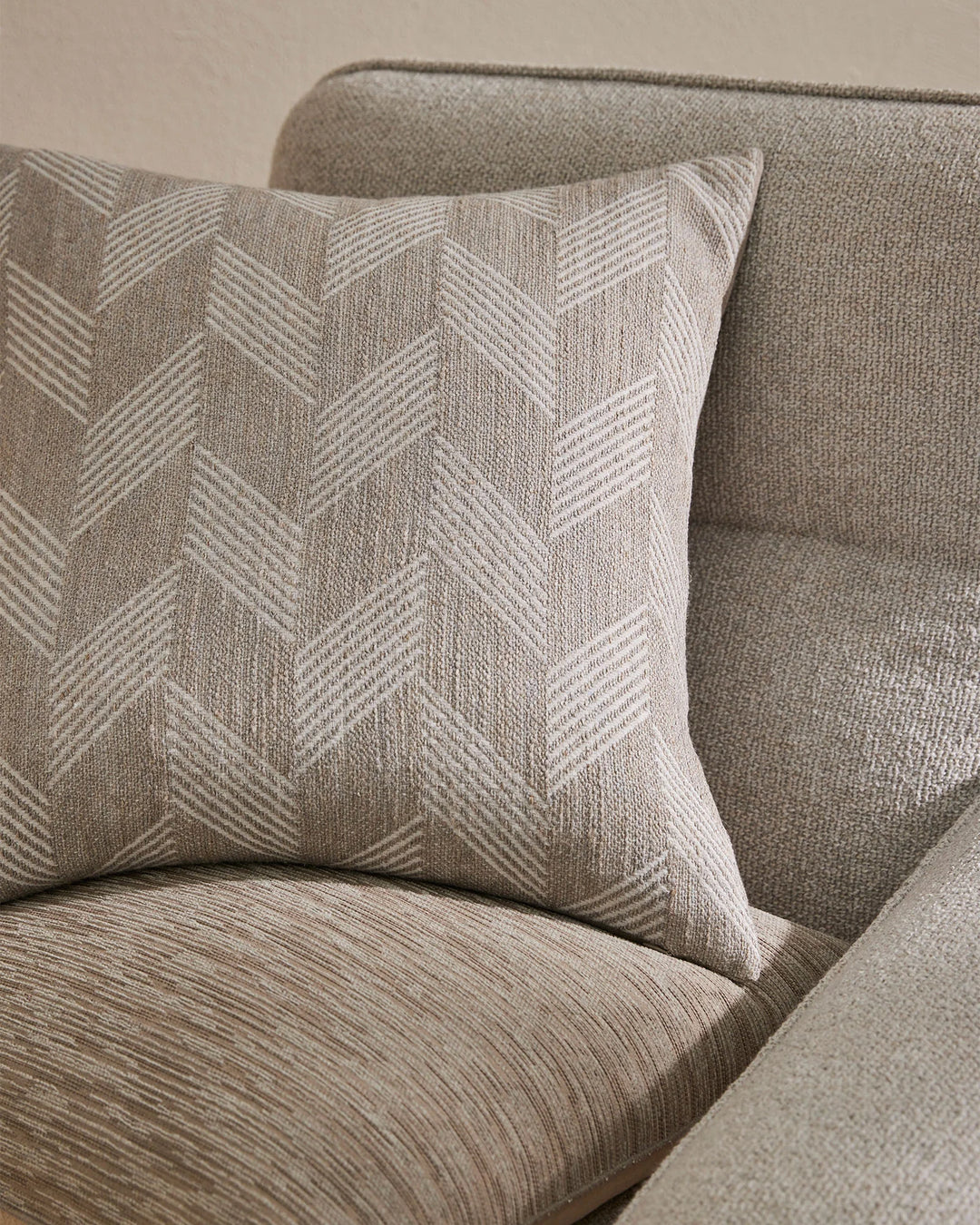 Neutral linen cushions with chevron weave texture styled on a soft taupe upholstered sofa, showcasing minimalist layering and tonal fabric interplay