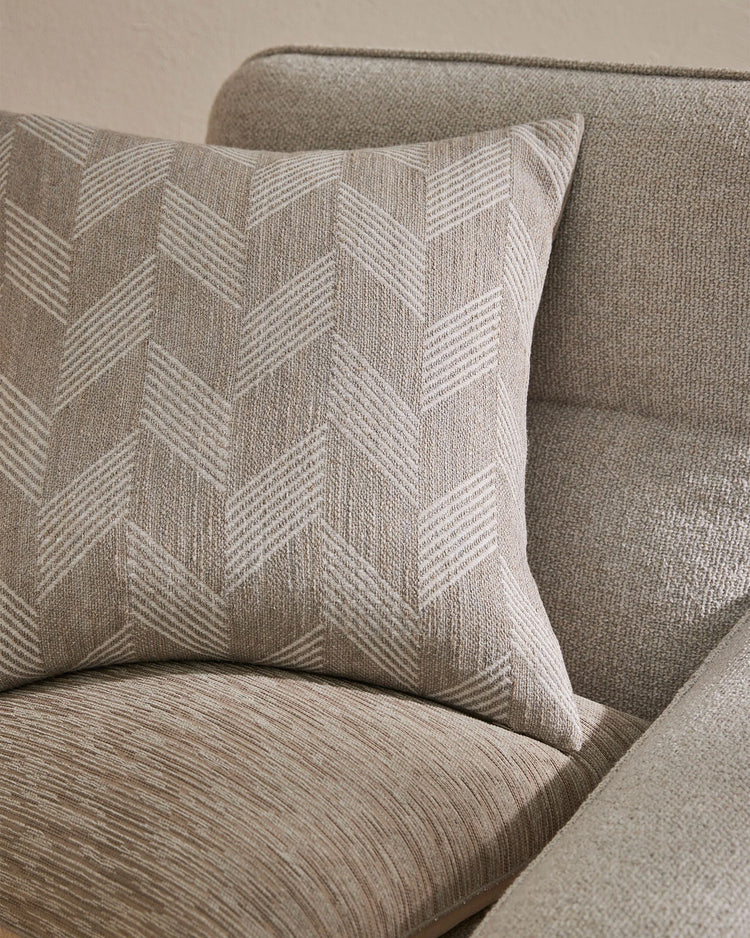 Neutral linen cushions with chevron weave texture styled on a soft taupe upholstered sofa, showcasing minimalist layering and tonal fabric interplay