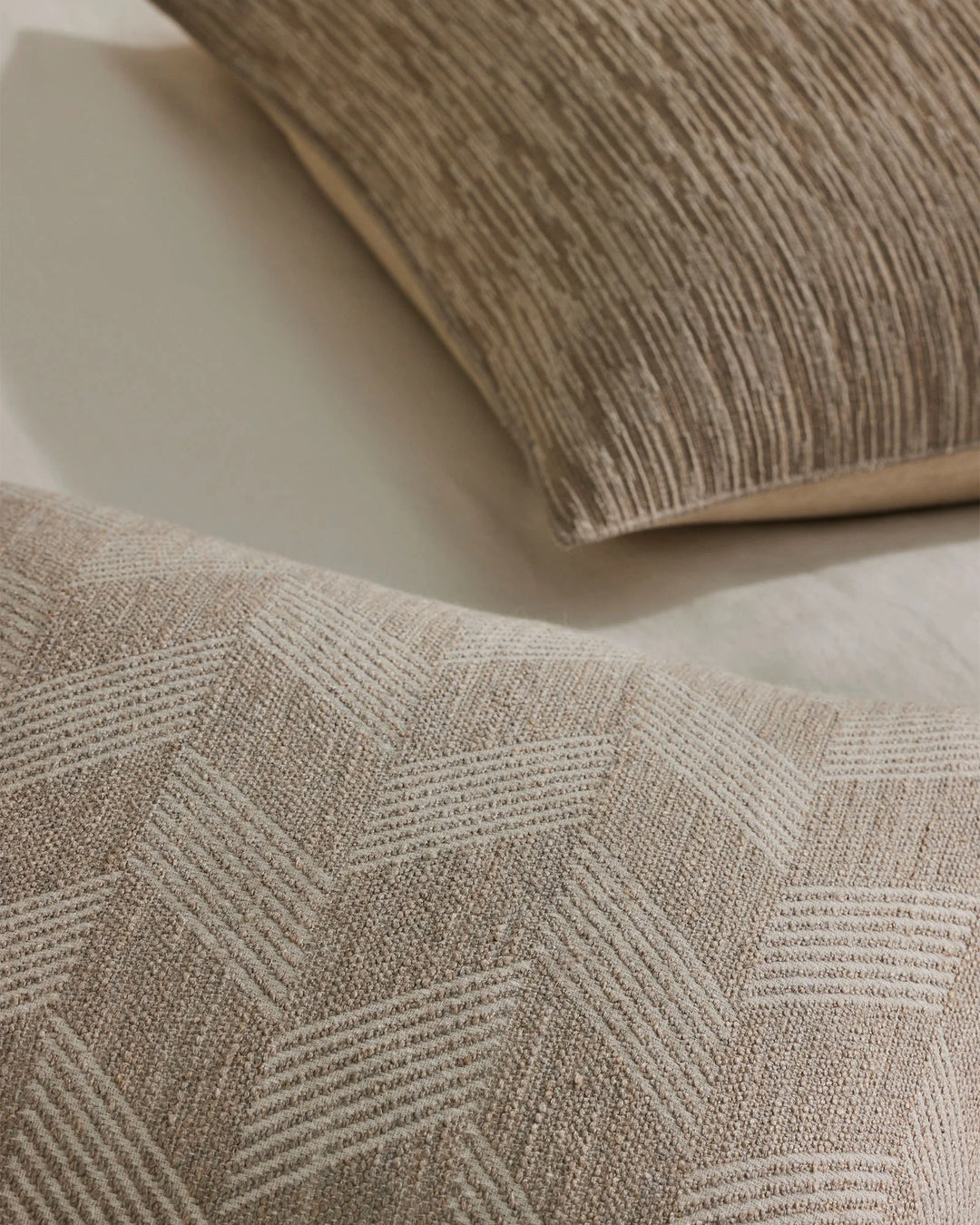 Neutral textured cushions styled flat lay, showcasing geometric line pattern weave in warm taupe and cream tones with linen blend fabrics
