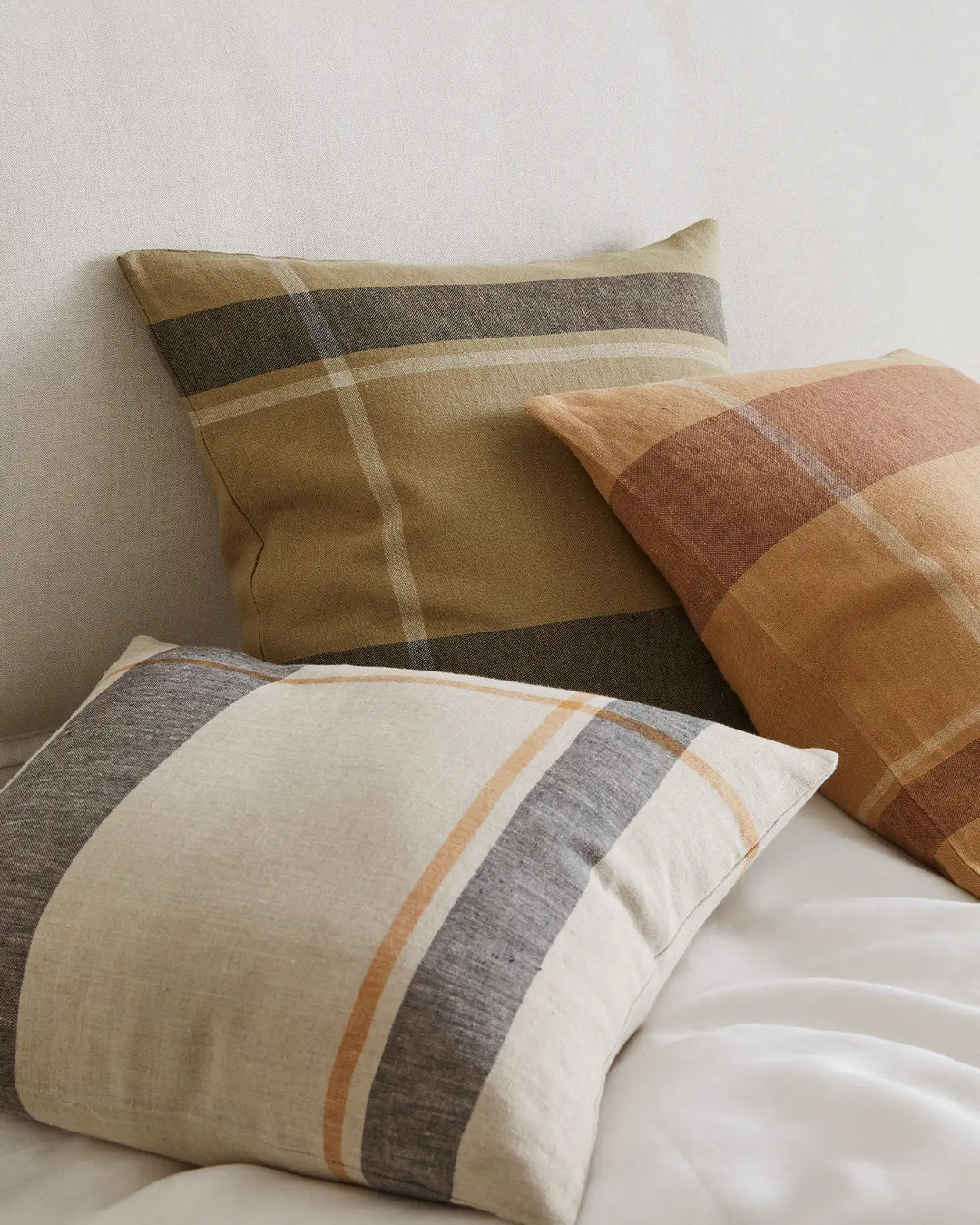 Stacked linen cushions in warm earth tones and neutral stripes, featuring terracotta, sage, and charcoal bands on natural bedding
