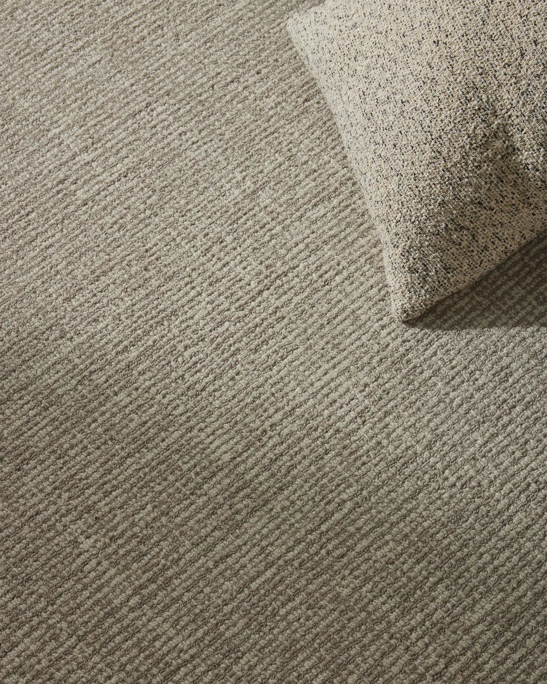Neutral textured wool rug layered in a monochromatic interior, showcasing ribbed weave patterns and soft cream-to-taupe palette for minimal, understated home styling