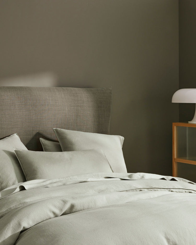 Sage green bedroom with linen Ravello bedding layered in soft naturals, textured upholstered headboard, wooden nightstand and pendant lamp creating calm minimalist aesthetic