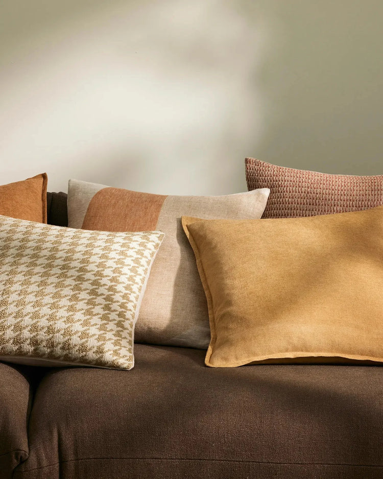 Warm earth-tone cushion layering on charcoal sofa featuring honey and terracotta hues, textured linens, and geometric patterned throws in neutral palette