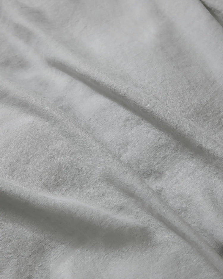 Close-up of silver Ravello flat sheet showing soft crumpled linen texture and natural light play on neutral bedding fabric