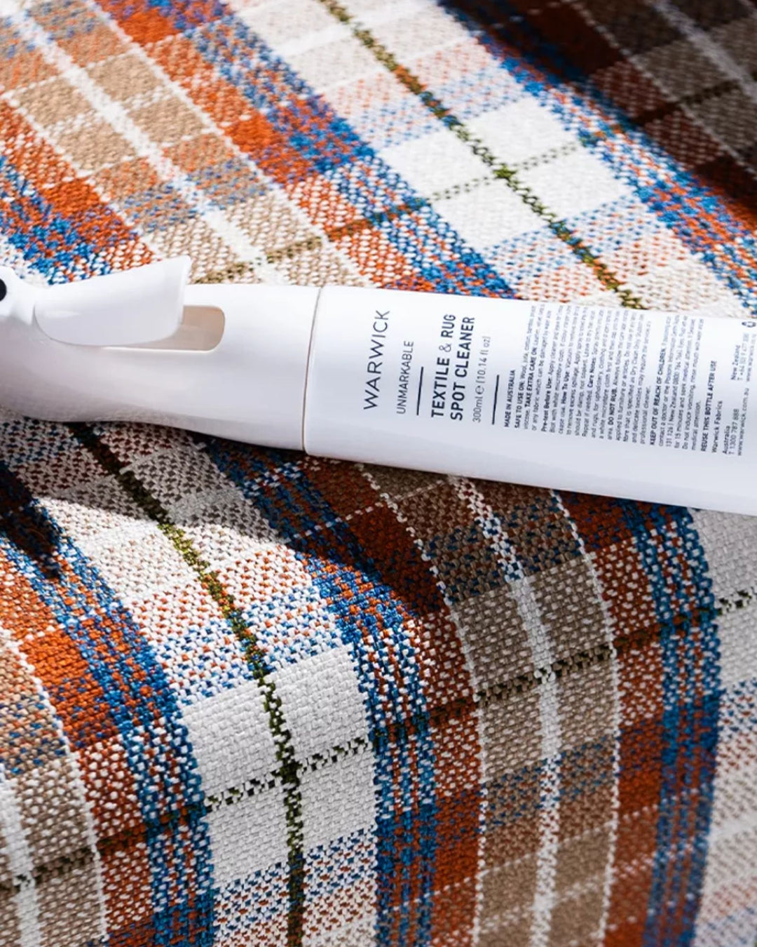 Unmarkable Textile & Rug Spot Cleaner spray bottle displayed on multicoloured patchwork rug with orange, blue and natural weave detailing by Weave Home