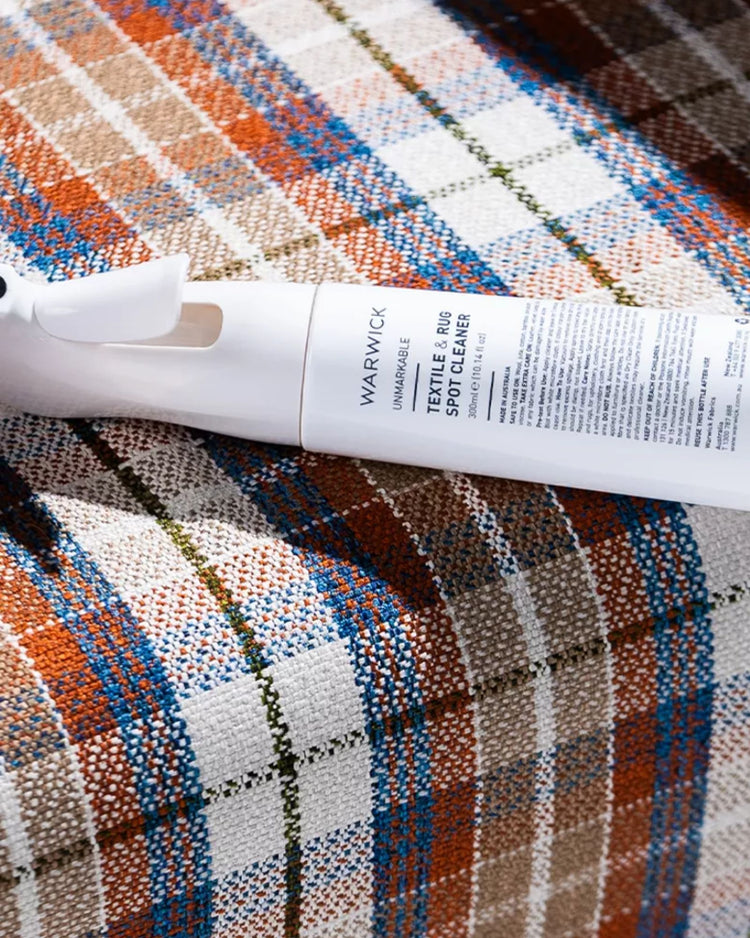 Unmarkable Textile & Rug Spot Cleaner spray bottle displayed on multicoloured patchwork rug with orange, blue and natural weave detailing by Weave Home