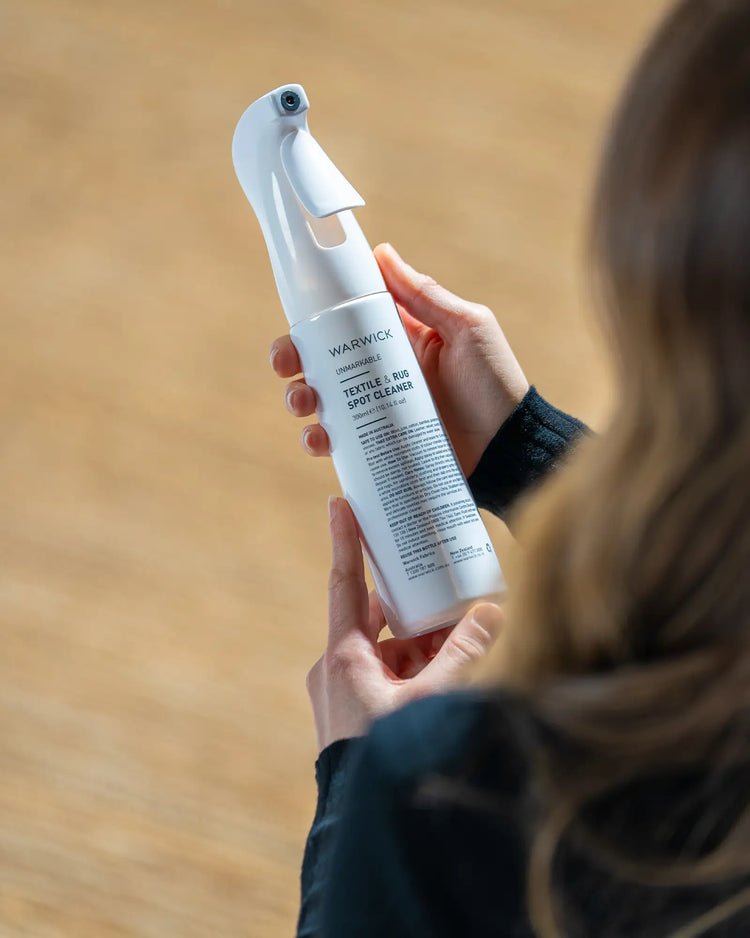 Warwick Unmarkable Textile & Rug Spot Cleaner spray bottle held in hand, white finish with trigger nozzle, by Weave Home