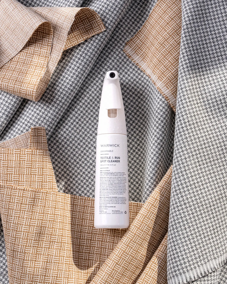 Warwick Unmarkable Textile & Rug Spot Cleaner spray bottle displayed on layered geometric woven textiles in neutral tones by Weave Home