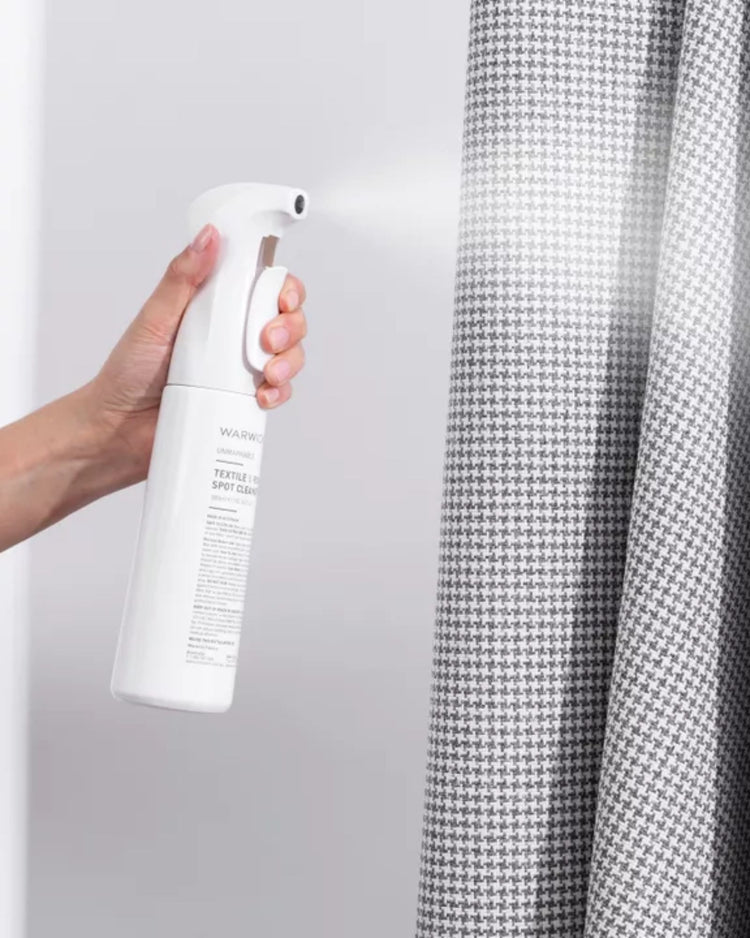 Unmarkable Textile & Rug Spot Cleaner spray bottle, white, held in hand with grey houndstooth fabric in background by Weave Home