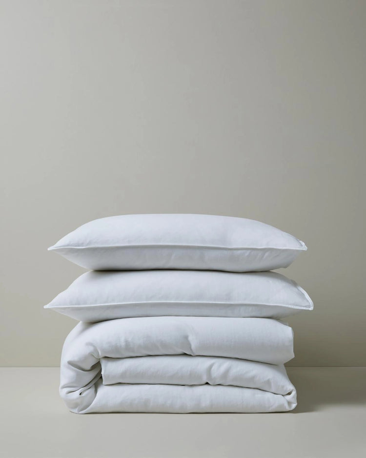 Stacked white linen bedding in minimalist aesthetic, featuring Ravello quilt cover and pillowcases with soft natural texture against neutral backdrop