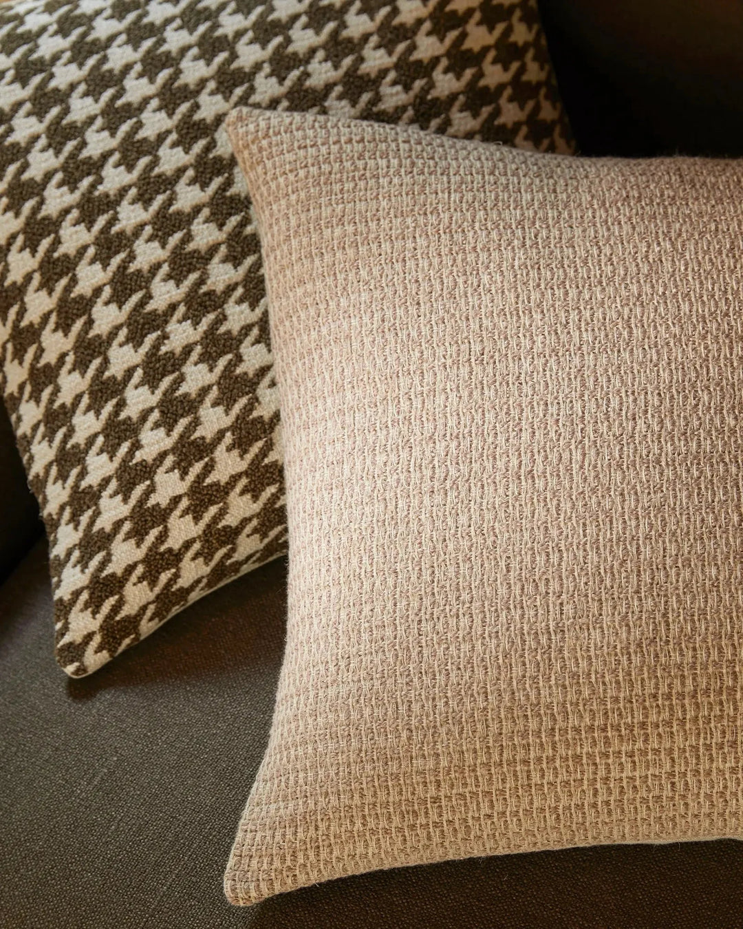 Neutral cushion styling with houndstooth pattern and textured linen weave, layered in warm taupe and cream tones on charcoal upholstery for contemporary interior design