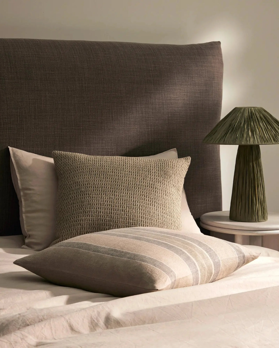 Neutral bedroom styling with textured linen cushions, striped pillow, and earthy toned headboard creating a calm, minimalist aesthetic with warm natural light