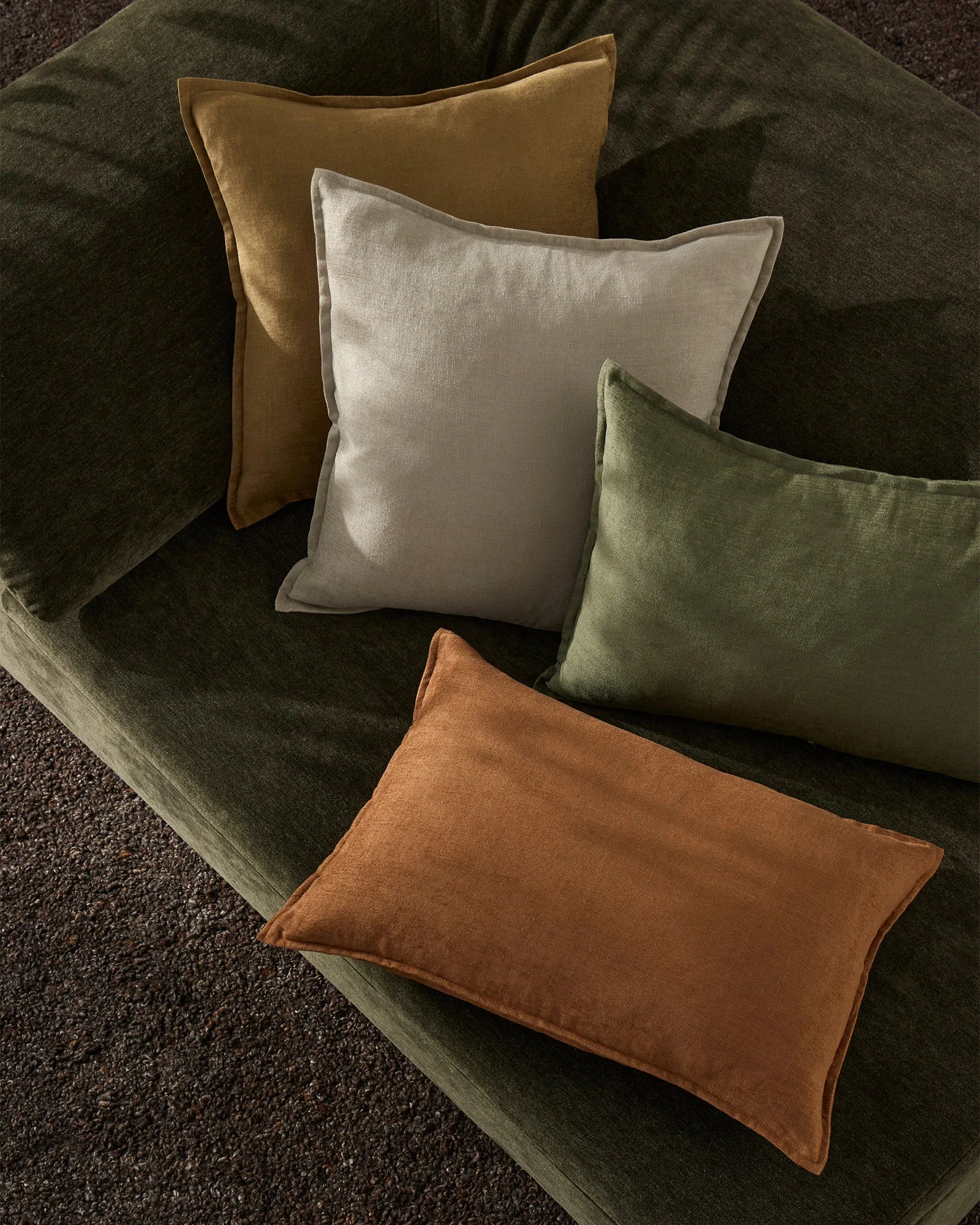 Earthy toned Fiore cushions in ochre, breeze and olive arranged on a charcoal sofa, layering warm terracotta and natural linen textures for a contemporary botanical aesthetic
