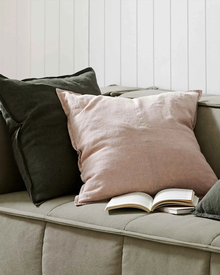 Neutral lounge with blush linen cushion and charcoal throw, open book on sage upholstery, white shiplap wall backdrop, relaxed reading nook styling