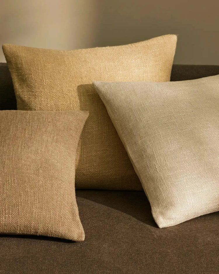 Neutral linen viscose cushions in sand, natural and clay tones layered on charcoal upholstery, textured weave detail and warm earthy palette for minimalist interior styling