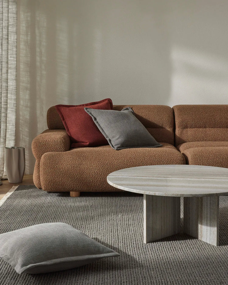 Warm minimalist living room with caramel linen sofa, layered Figlio cushions in paprika and graphite, grey wool rug, and soft natural light from linen curtains