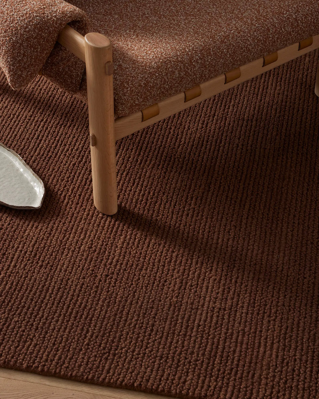 Warm terracotta wool rug styled with natural wood bed frame and layered textiles, creating earthy, minimalist bedroom aesthetic with rich texture and neutral palette.