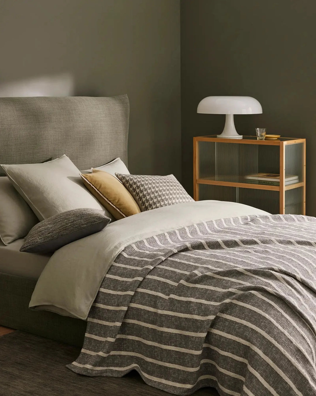Sage green bedroom with Piazza throw in striped linen, layered with cream and gold cushions, textured Giovanni cushion, and neutral bedding for contemporary minimalist style