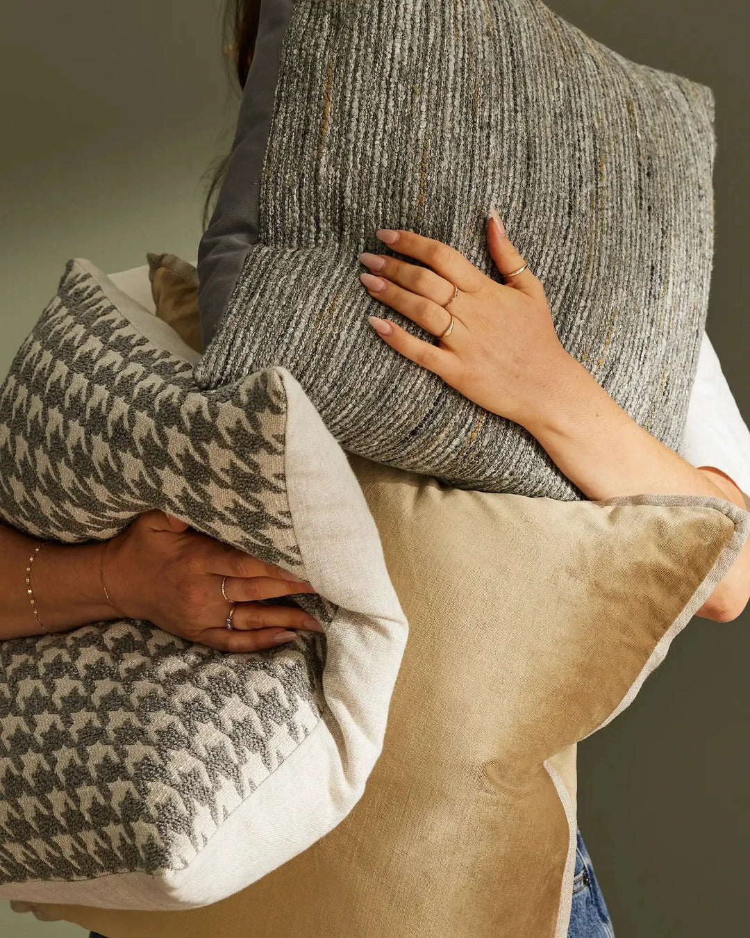 Neutral earth-tone cushions in ribbed and geometric patterns stacked together, showcasing layered textures in sage, taupe and cream with natural linen details