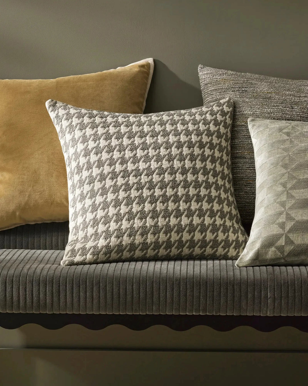 Neutral living room styling with layered cushions in sage and cream tones—textured quilted and geometric jacquard patterns with warm ochre velvet accent on grey ribbed sofa