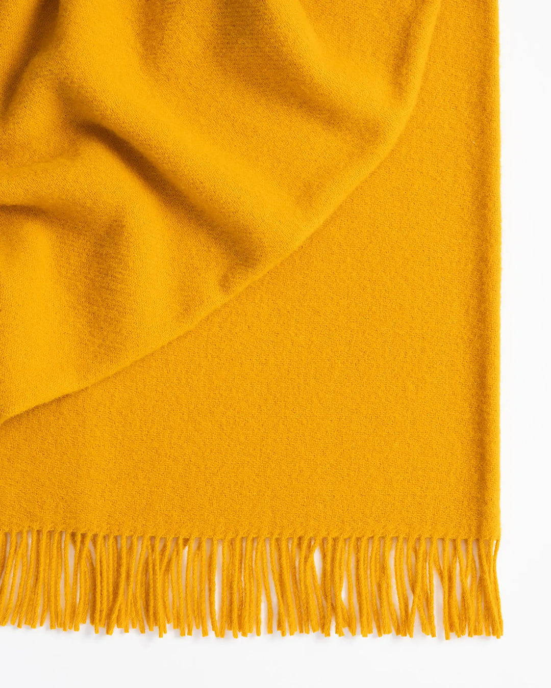 Nevis Saffron lambswool throw detail, showing warm yellow wool with tassel fringe border by Weave Home