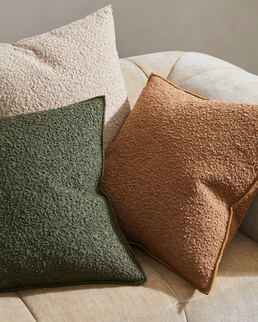 Earthy tone cushion styling with olive, copper and nougat Alberto cushions on a cream upholstered sofa, showcasing layered neutral and warm palette with textured weave fabrics
