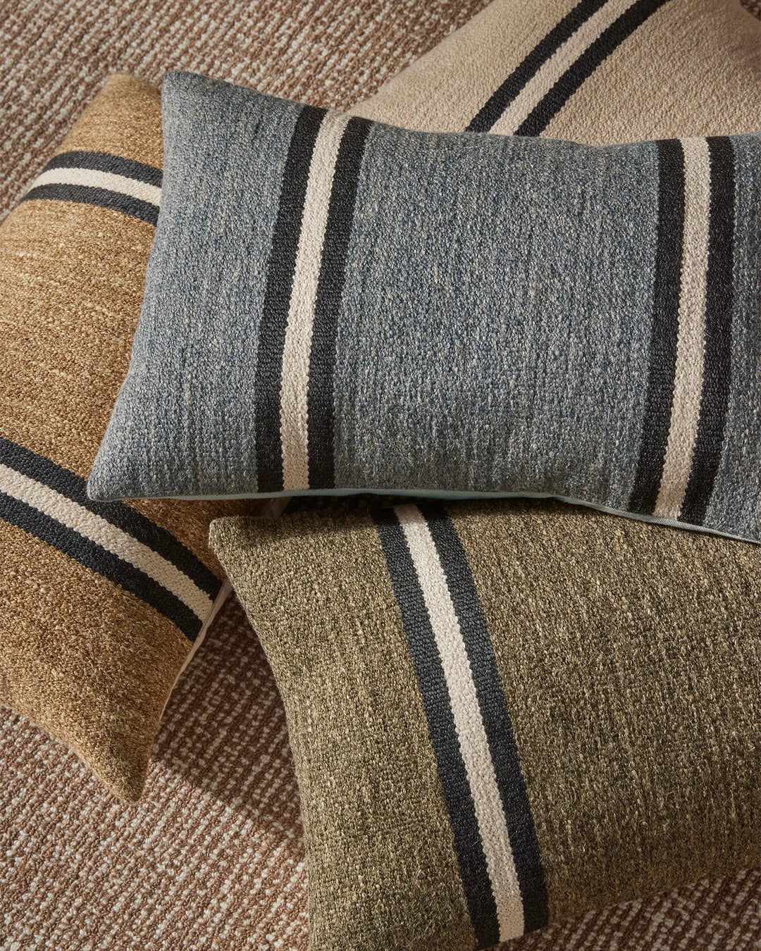 Neutral striped cushions in forest green, sage and warm sand tones layered on textured natural linen, creating an earthy, minimalist aesthetic for coastal and contemporary home styling.