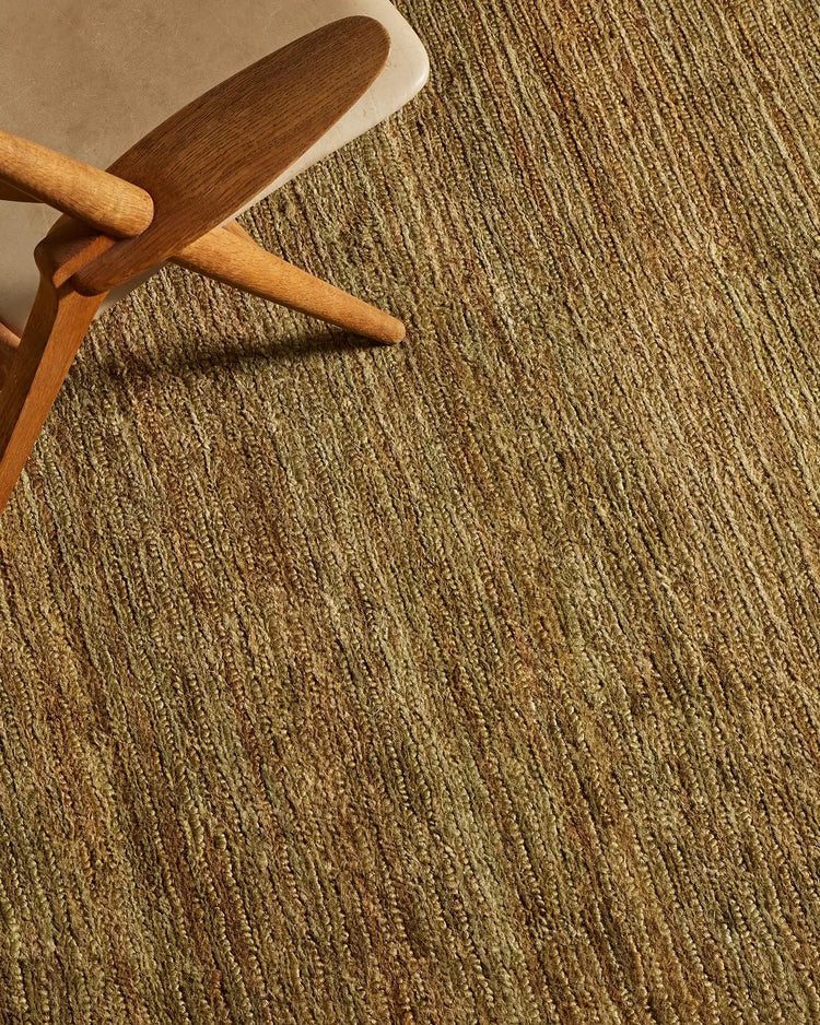Warm wood chair frame and mid-century accent piece styled on natural jute textured rug in earthy oakmoss tone, creating layered neutral aesthetic