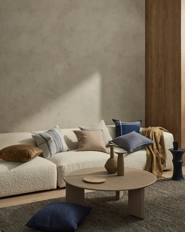 Minimalist living room with cream boucle sofa styled with navy, ochre and neutral striped cushions in linen and viscose, warm wood accents and natural light casting geometric shadows