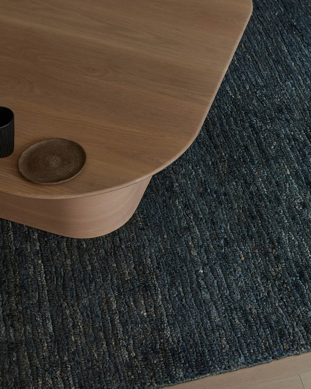 Warm timber furniture and bronze accent vessel on charcoal textured jute rug, contemporary minimalist styling with natural materials and neutral palette