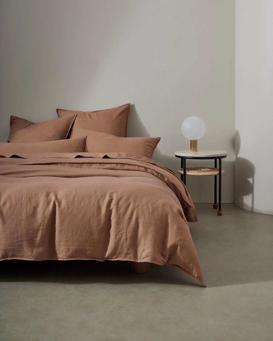 Minimalist bedroom with warm terracotta linen bedding layered on a bed, featuring European linen texture and relaxed styling against neutral walls and a simple side table