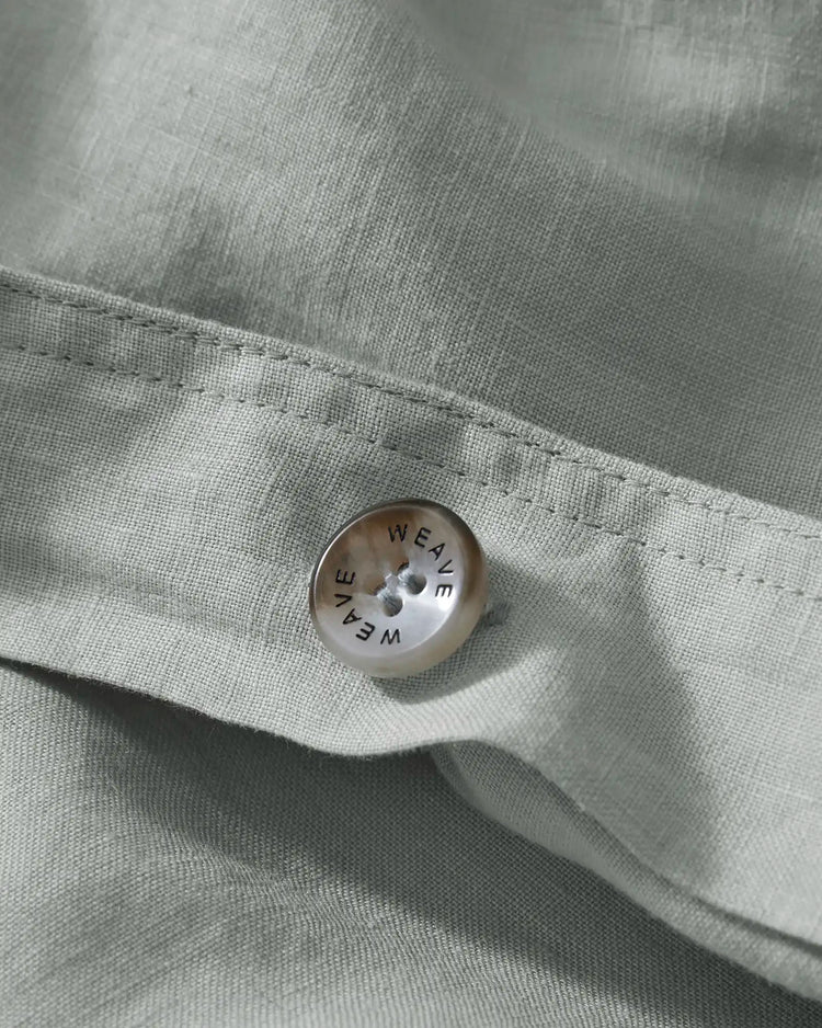 Ravello Quilt Cover button detail in sage, showing branded Weave Home closure button on European linen fabric with blanket stitch seam