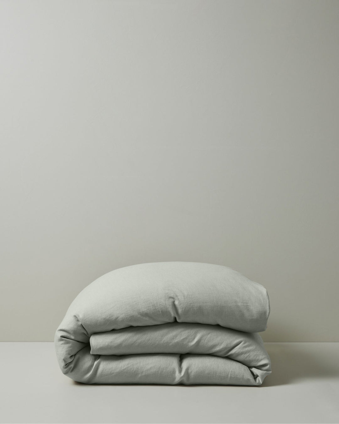 Ravello Quilt Cover in Sage, European linen rolled in soft folded layers against neutral background by Weave Home