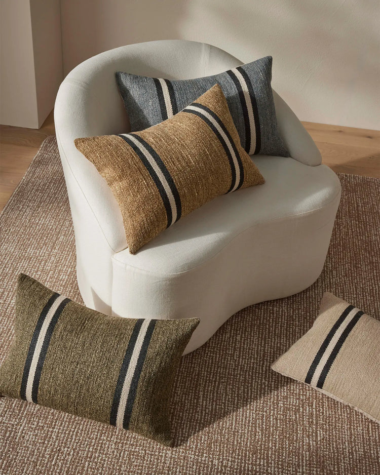 Striped cushions in caramel, grey and olive on cream curved chair with textured neutral rug, showcasing contemporary Scandinavian home styling