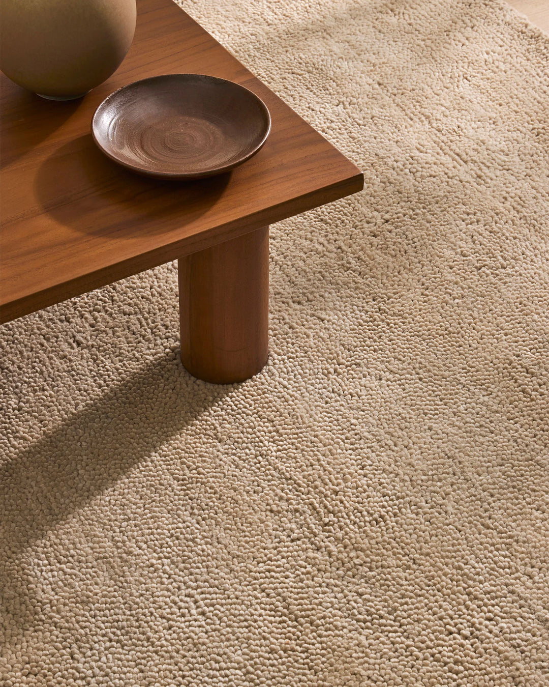 Warm beige wool rug layered under timber coffee table with ceramic bowl and ceramic vessel, earthy minimalist interior styling